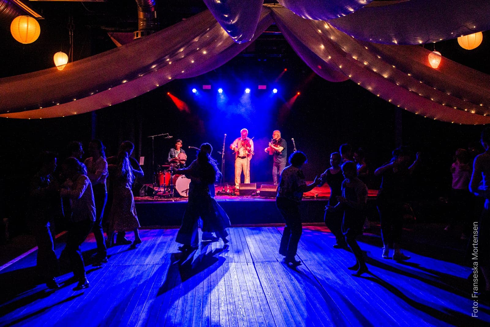 Dancers in silhouette on the blue-lit dance floor as BOOT play beneath the fabric drapes