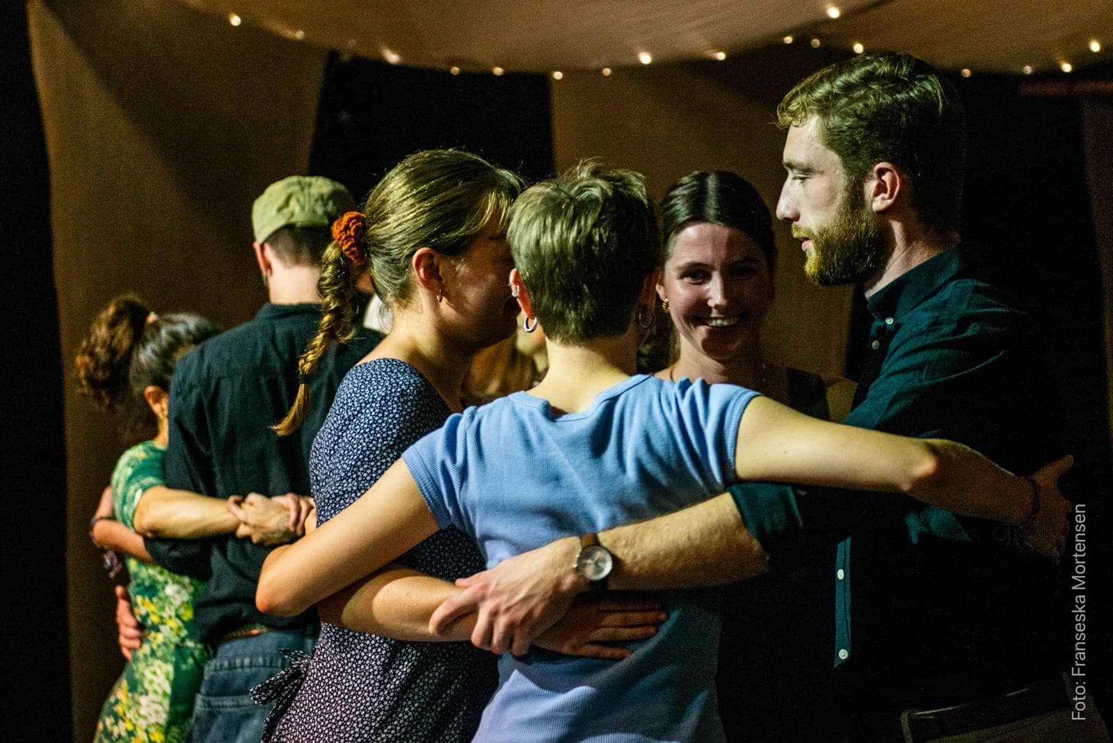 Dancers with their arms around each other in a close circle, smiling on the dance floor