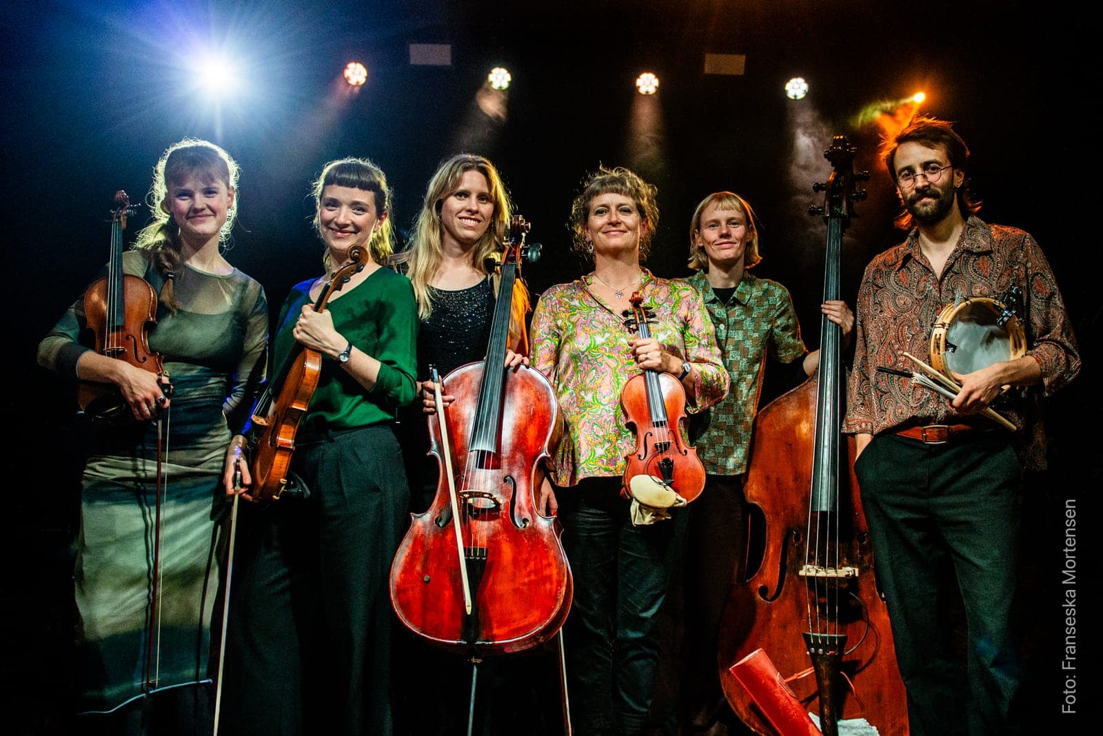 The musicians of Det Lyse Bal together on stage with violins, cello, double bass and a frame drum