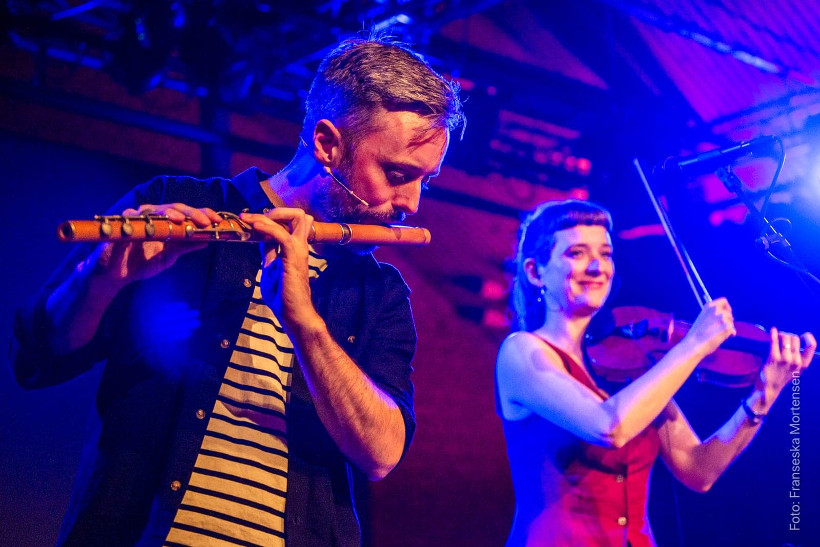 The flute player and the smiling fiddler of Floating Sofa Quartet playing side by side in blue and red light