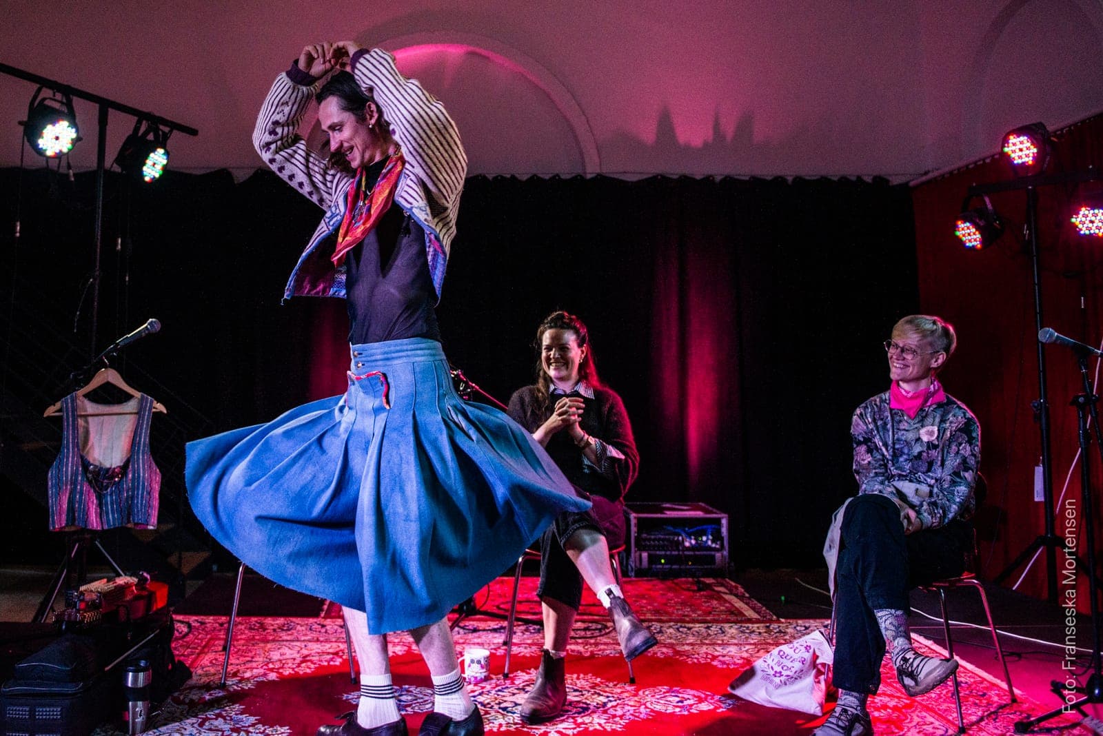Fredy Clue twirling in a blue skirt as the two conversation partners watch, smiling