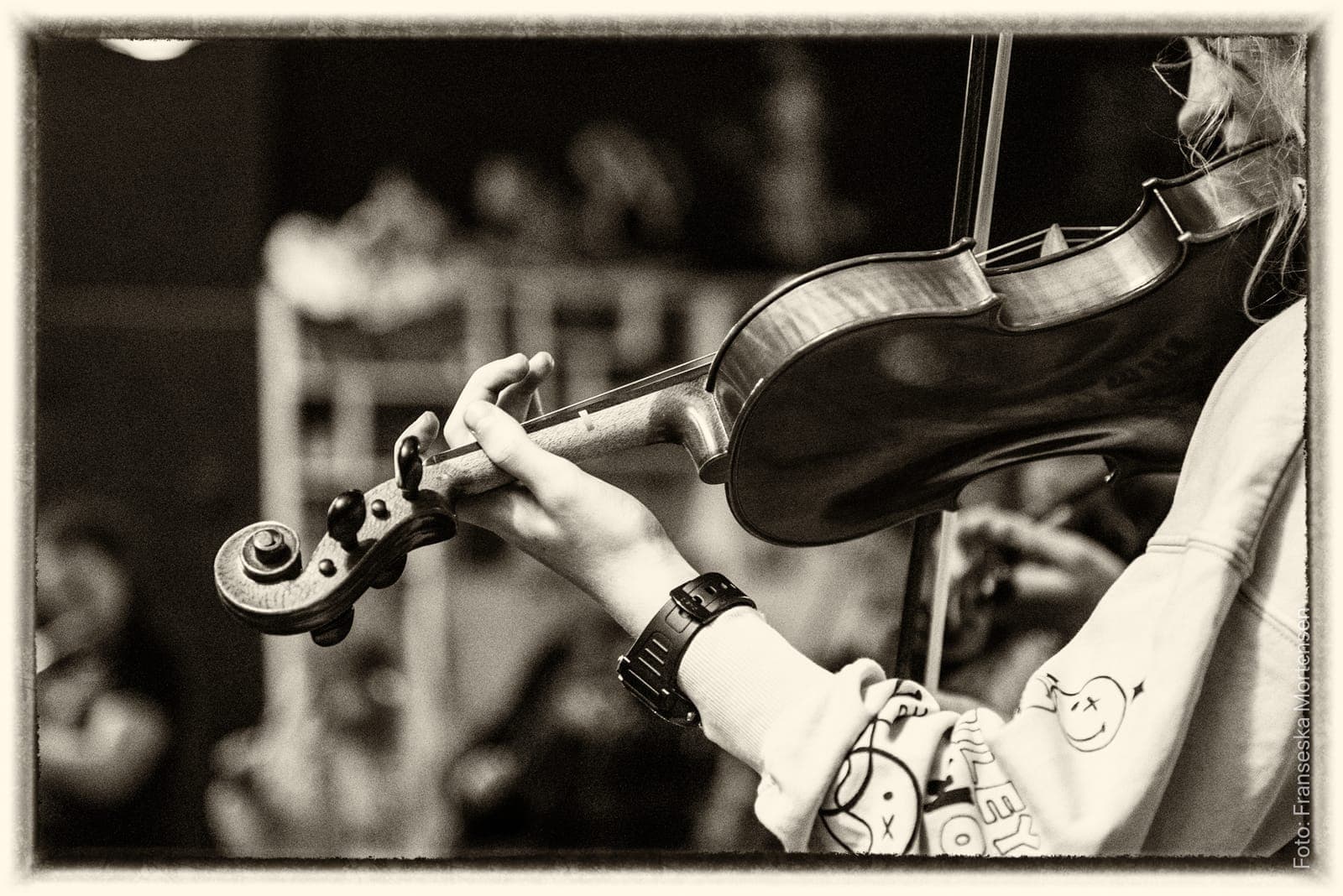 Black-and-white close-up of a young violinist's hand on the neck of the violin