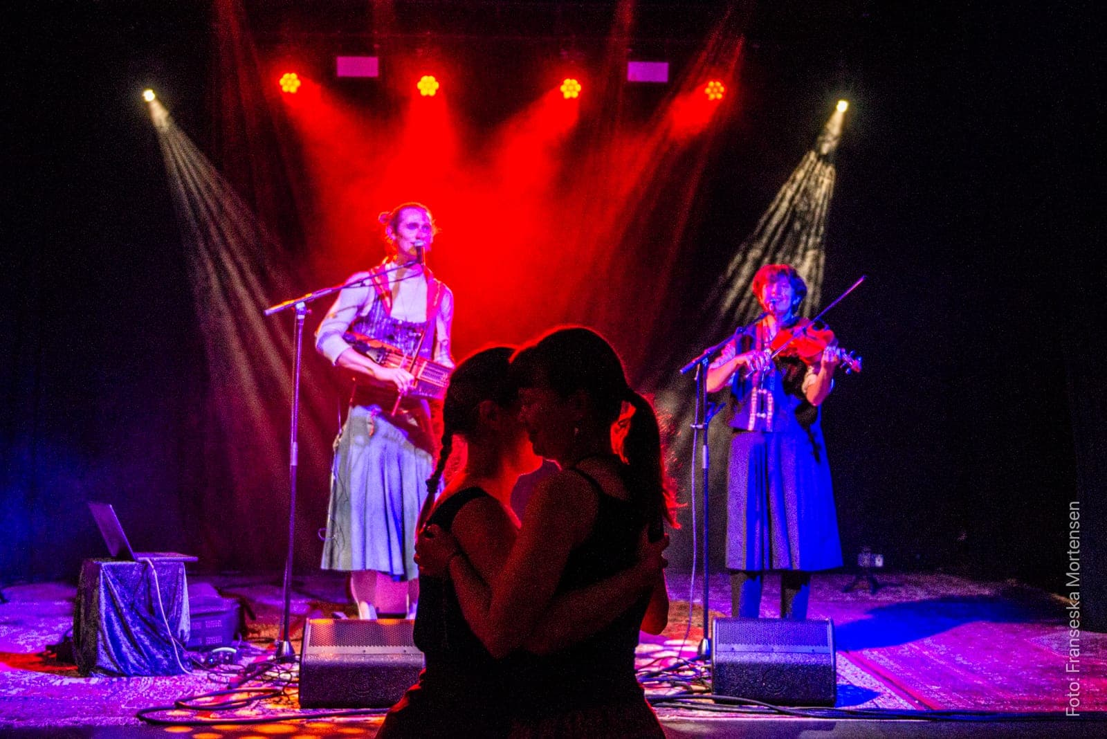 A couple dancing close in silhouette in front of Fredy Clue and Julia Bengtson on stage