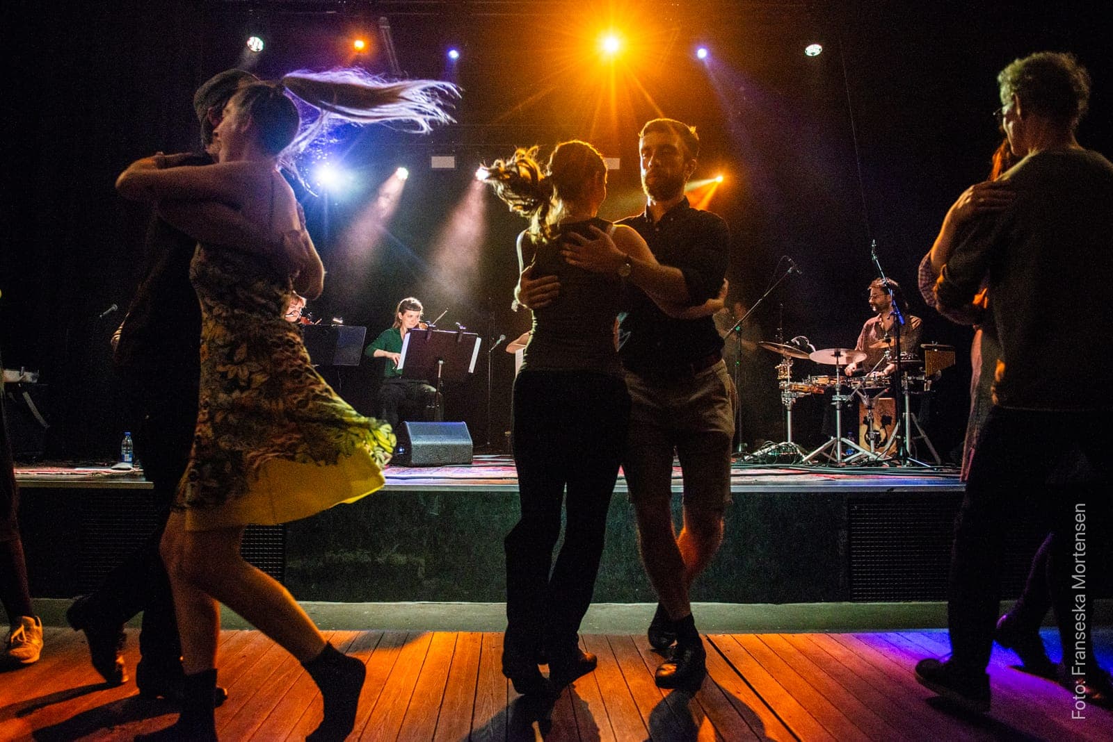 A couple spinning so fast that hair flies, in warm stage light in front of the musicians