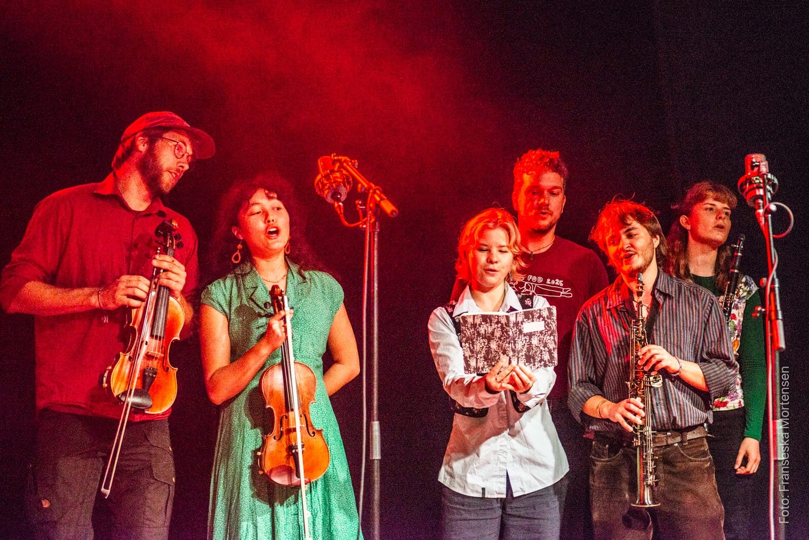 Young musicians from Rod and Fod singing and playing fiddles and clarinet in red stage light