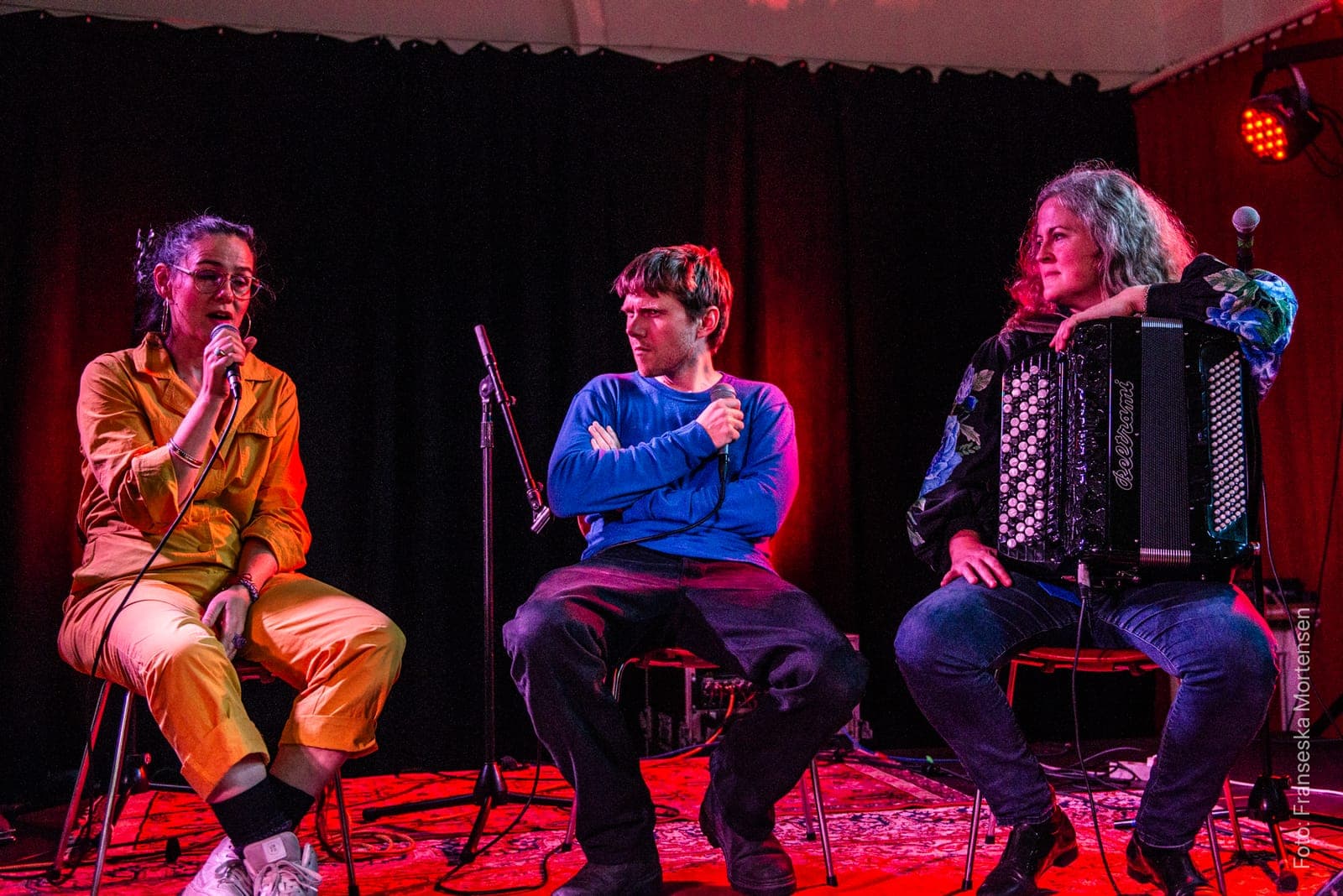 Jullie Hjetland, the host and Mette Kathrine Stærk with an accordion seated on the FOLK stage in front of a red curtain
