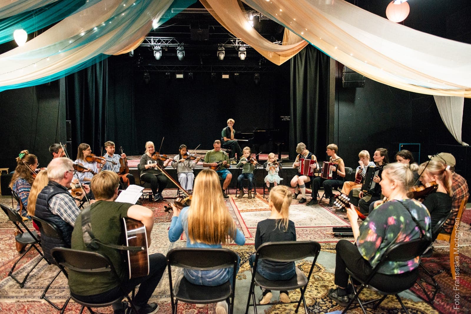 Musikere i alle aldre spiller violin, mandolin, guitar og harmonika sammen i en stor rundkreds
