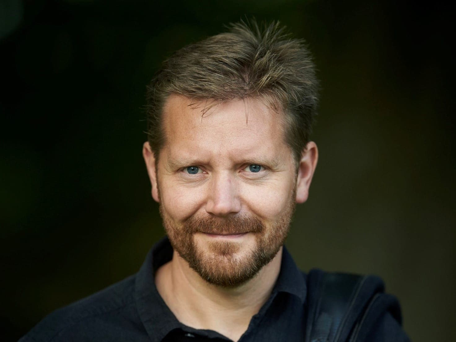Portræt af Jesper Vinther Petersen i mørk skjorte mod en mørkegrøn baggrund