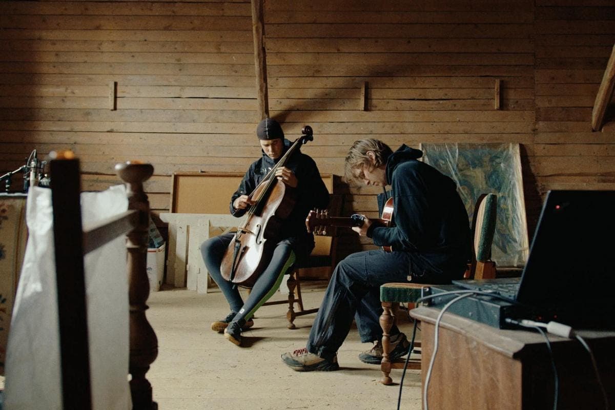 Geo Pjäsernas to musikere spiller cello og guitar i et rum med trævægge