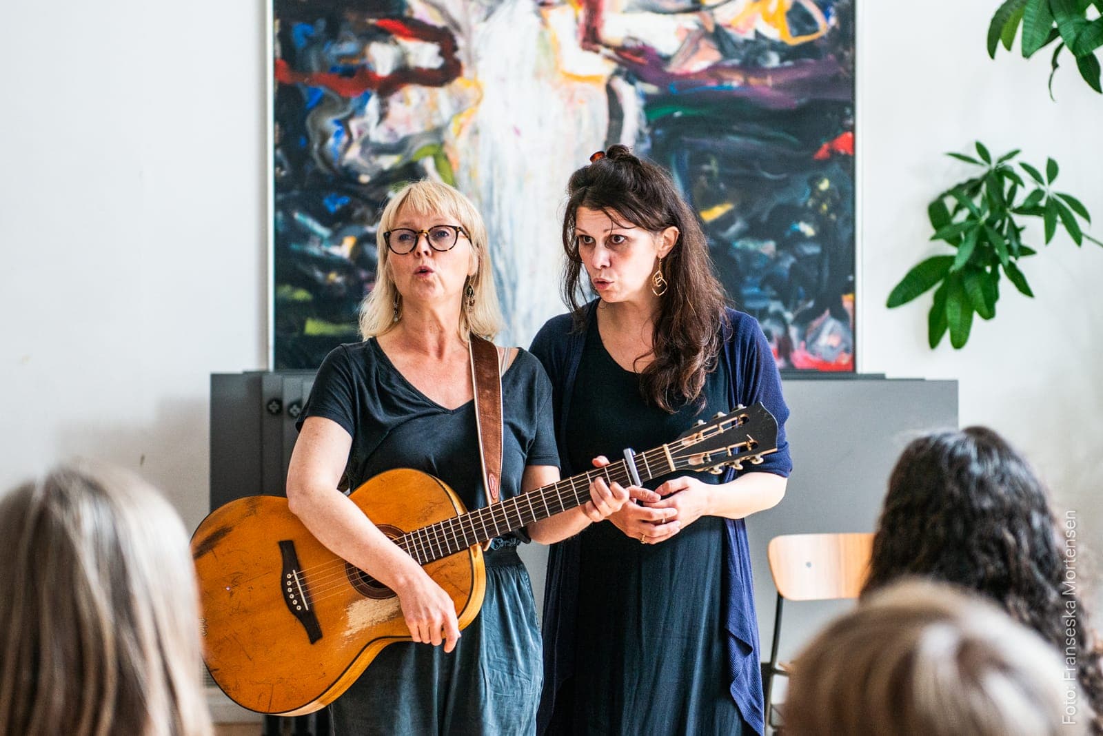 To sangere synger sammen til en sangworkshop i et lyst lokale, den ene med guitar