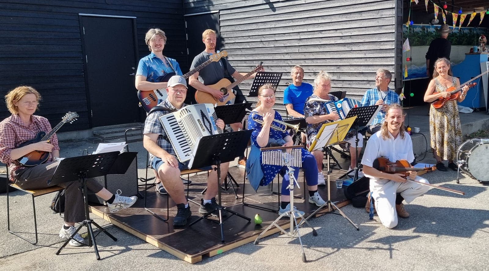 Skidtspils musikere samlet udendørs med violiner, harmonikaer, guitar, bas og percussion